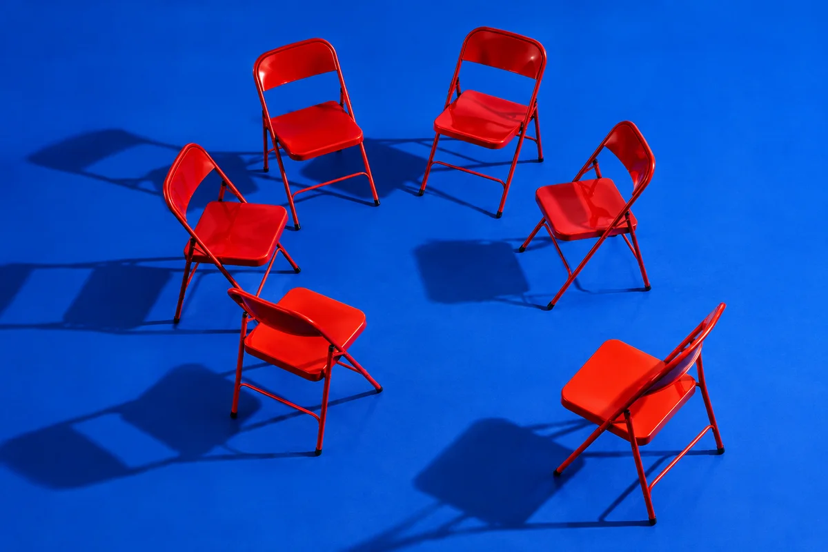 Red folding chairs form an open circle on a cobalt blue floor.